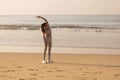 Fit young adult woman in work out clothing stretching hands and body on the beach in the morning Royalty Free Stock Photo