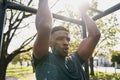 Fit young black man in t-shirt doing pull-up on monkey bars in park