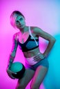 Fit young blonde woman posing with medicine ball in gym in neon lights. Royalty Free Stock Photo