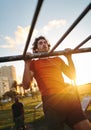 Fit young man with earphones in his ears training his arms muscles on bars at outdoors gym in summer - man doing pullups Royalty Free Stock Photo