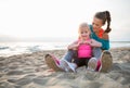 Fit young mother and daughter sitting on the beach at sunset