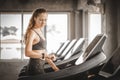 Fit young woman caucasian running on machine treadmill workout in gym. Glad smiling girl is enjoy with her training process.