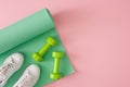 Creative composition of dumbbells, green exercise mat and white sports shoes on pastel pink background