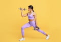Fitness african american woman training with two dumbbells, doing lunges exercises for leg muscle on yellow background Royalty Free Stock Photo