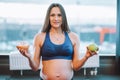 Fitness attractive pregnant woman in sportswear. Doing yoga exercise, choise green apple, donut. Diet starving. Close up