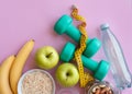 Fitness background with bottle of water, apple, dumbbells, nuts, and tape measure on pink tableÃÅ½ Royalty Free Stock Photo