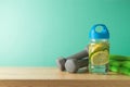 Fitness background with infused lemon and cucumber water, towel and dumbbells on wooden table