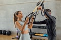 Coach helps concentrated woman with suspension strap workout at gym hiit class. Royalty Free Stock Photo