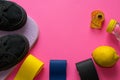 Fitness composition of colorful elastic gum expanders, fresh lemon juice, measuring tape, black sneakers on pink background with