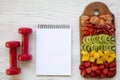 Fitness concept, diet plan. chopped fruits, dumbbells , notepad on white wooden background,