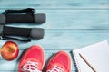 Fitness concept, pink sneakers, red apple, dumbbells and notebook with pencil on wooden background, top view Royalty Free Stock Photo