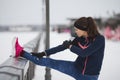 Fitness concept - sport girl model runner doing flexibility exercise for legs before run at snow winter promenade Royalty Free Stock Photo