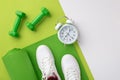 Fitness concept. Top view photo of white sneakers over green exercise mat dumbbells and alarm clock on bicolor green and white Royalty Free Stock Photo