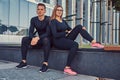 Fitness couple in a sportswear, blonde girl and a handsome muscular guy sitting on a bench against a skyscraper. Royalty Free Stock Photo