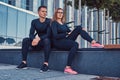 Fitness couple in a sportswear, blonde girl and a handsome muscular guy sitting on a bench against a skyscraper. Royalty Free Stock Photo