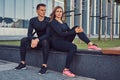 Fitness couple in a sportswear, blonde girl and a handsome muscular guy sitting on a bench against a skyscraper. Royalty Free Stock Photo