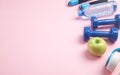 Fitness equipment. Dumbbells, apple, headphones, water bottle on pink background