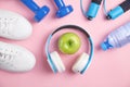 Fitness equipment. Dumbbells, apple, headphones, water bottle on pink background