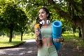 Active young indian woman with yoga mat and water bottle in park setting Royalty Free Stock Photo
