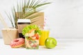 Fitness food set of coffee, orange juice, shrimp salad, noodles in box, donut, apple, packet in white interior, palm leaf. Mockup. Royalty Free Stock Photo