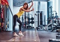 Fitness girl posing for a camera while leaning on a barbell in the modern gym Royalty Free Stock Photo