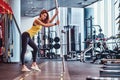 Fitness girl posing for a camera while leaning on a barbell in the modern gym Royalty Free Stock Photo