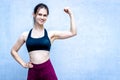 Fitness girl in sportive top shows muscules - blue wall copy space