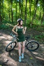 Fitness girl wear green dress rides a modern mountain bike in forest at hot summer day Royalty Free Stock Photo