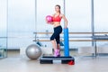 Fitness girl, wearing in sneakers, red top and black breeches, posing on step board with ball, the sport equipment Royalty Free Stock Photo