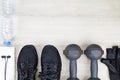 Fitness grove, drinking water bottle, sport shoes, dumbbells, white towel and headphone on wooden background