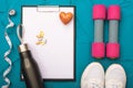 Fitness at home - sheet of paper with a pen and white sneakers, dumbbells and measuring tape, bottle with water and vitamins Royalty Free Stock Photo