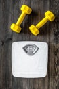 Fitness for losing weight. Bathroom scale and dumbbell on wooden background top view Royalty Free Stock Photo