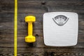 Fitness for losing weight. Bathroom scale, measuring tape and dumbbell on wooden background top view Royalty Free Stock Photo