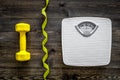 Fitness for losing weight. Bathroom scale, measuring tape and dumbbell on wooden background top view Royalty Free Stock Photo