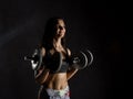 Fitness girl with dumbbells on a dark background. Athlete doing exercises in the gym Royalty Free Stock Photo