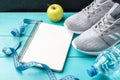 Fitness sneakers, green apple, measure tape, bottle of water and notebook on blue wooden background Royalty Free Stock Photo