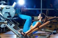 Fitness, sport, bodybuilding, exercising and people concept - young woman flexing muscles on leg press machine in gym Royalty Free Stock Photo