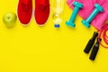 Fitness and sport concept. Jump rope, green apple, dumbbells, bottle of water, red sneakers and pink towel on bright yellow Royalty Free Stock Photo