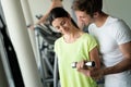 Smiling young woman and personal trainer with dumbbells in gym Royalty Free Stock Photo