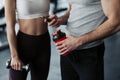 Fitness, sport, technology and slimming concept - close up of smiling young woman and personal trainer with smartphone and water