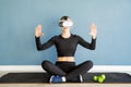 Young blonde woman in sport clothes wearing virtual reality glasses sitting at fitness mat using VR interactive menu