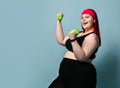 Fitness spring diet weight loss concept. Smiling winking plus-size overweight woman does exercises with weights dumbbells