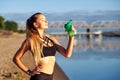 Fitness woman with bottle of water after running training on beach coast and morning urban city background