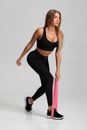 Fitness woman doing exercise for glutes with resistance band on gray background. Athletic girl working out