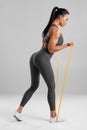 Fitness woman doing exercise with resistance band on gray background. Athletic girl working out