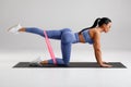 Fitness woman doing kickback exercise for glutes with resistance band on gray background. Athletic girl working out donkey kicks