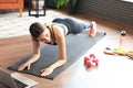 Fitness woman doing plank and watching online tutorials on laptop, training in living room. Stay at home activities