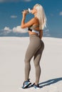 Fitness woman drinking water, outdoor. Athletic girl quenches thirst. Beautiful female in leggings with sexy butt