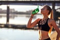 Fitness woman drinking of water after running training on beach coast and morning urban city background