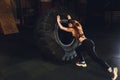 Fitness woman flipping wheel tire in gym. Fit female athlete working out with a huge tire. Back view. Sportswoman doing